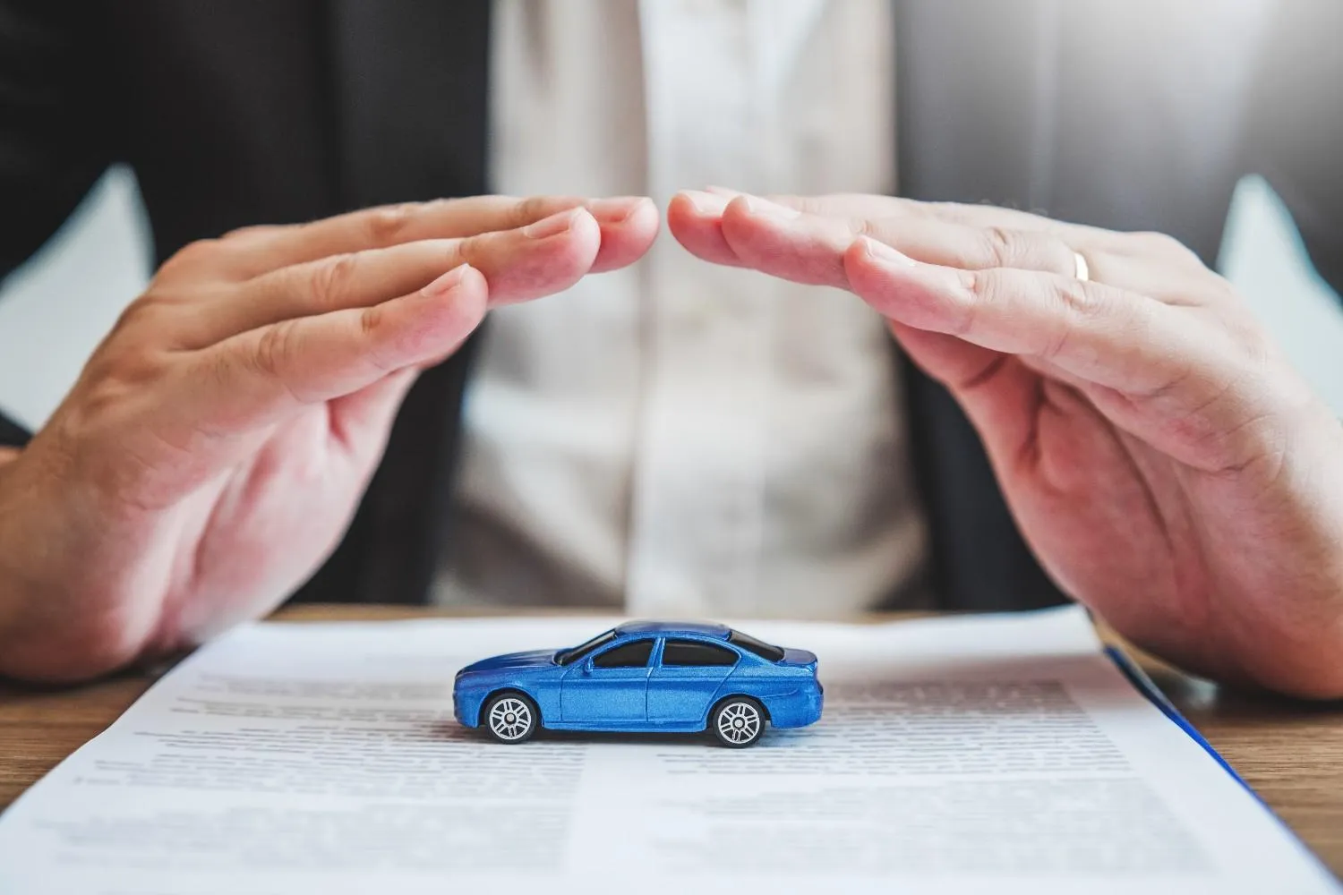 Two hands held over a toy car resting on an auto insurance policy