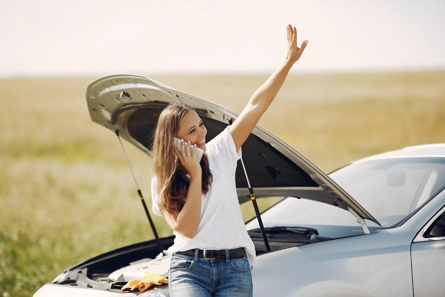 Driver waving for help beside her car with the hood open on a country road